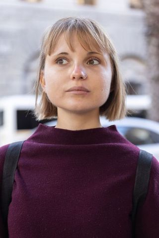 Young woman looking upward on urban sidewalk wearing maroon sweater and backpack