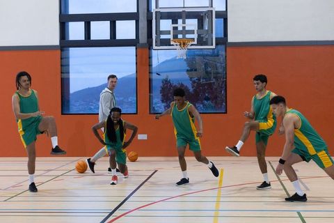Youth basketball team stretching with coach indoors