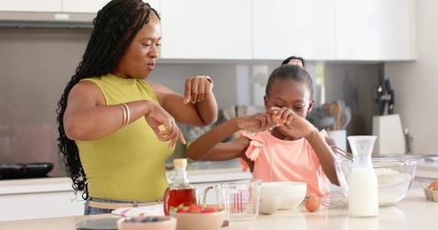 African american mother teaching daughter baking on kitchen island, mixing batter and bonding
