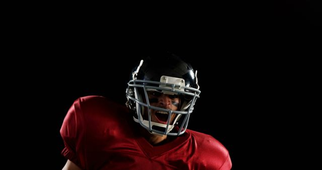Football player in red jersey and helmet shouting with intensity. Beneficial for use in sports promotions, advertisements for football equipment, team apparel, or motivational sports content.