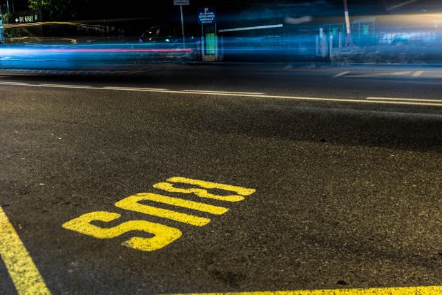 Night scene shows bus lane on a city street marked with yellow 'BUS' letters while traffic, captured with motion blur visualization, ages in width past lanes. Can illustrate guidelines or themes such as urban infrastructure, transport management regulations, city nightlife visibility or abstraction, also useful for blog article visuals.