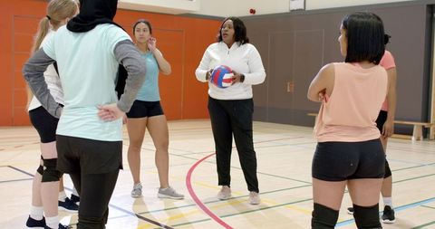 African american coach leading diverse women's volleyball team in gym training session