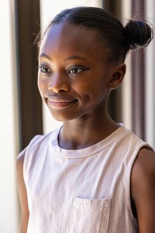 Sunlit african girl gazing out window, serene youth portrait with subtle smile and buns