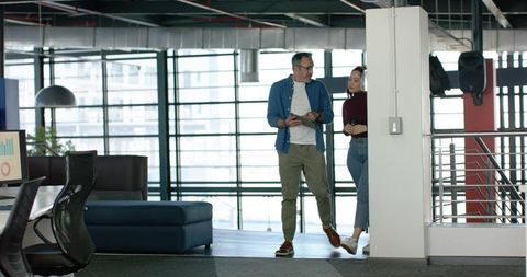 Diverse coworkers walking and discussing on mezzanine in modern open-plan workspace