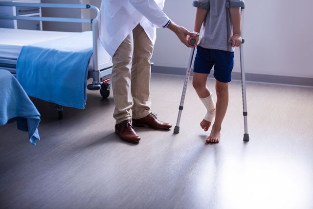 Doctor assisting injured boy to walk with crutches in hospital