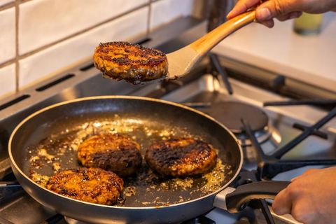 Home cook flipping seared burger patties in nonstick skillet on gas stove