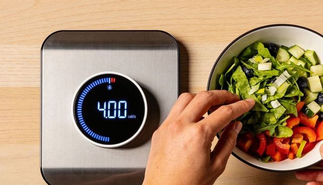 Hand tossing fresh salad on digital food scale displaying 4.00 for portion control