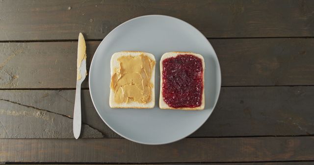 Close up view of peanut butter and jelly sandwich in a plate with butter knife on wooden surface. food and nutrition concept