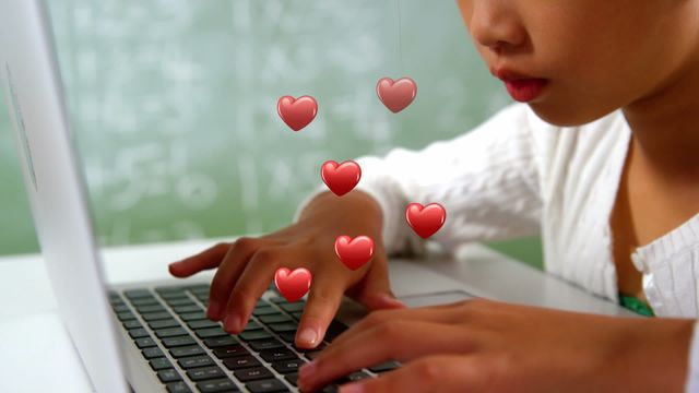 Young Asian girl concentrating while using a laptop with hearts symbolizing engagement and technology interaction. Ideal for illustrating modern classroom learning environments, digital education platforms, or showcasing positive technological interactions in schools. Suitable for educational publications, technology review articles, and school technology presentations.