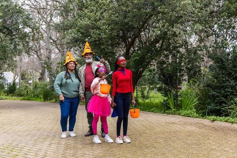 African american family trick-or-treating on neighborhood path wearing halloween costumes and pumpki