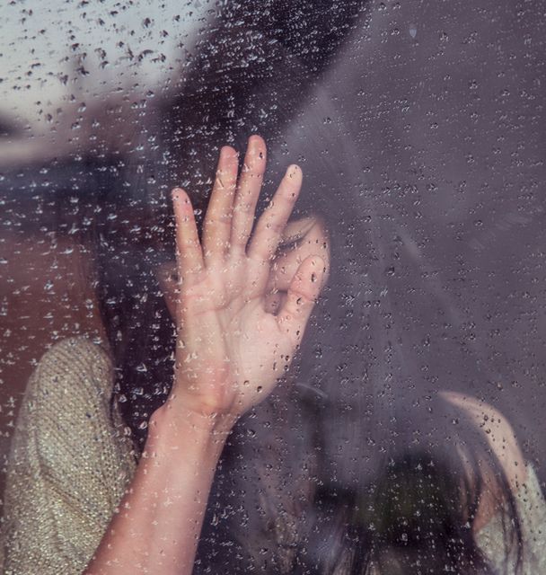 Person touching rainy window, signifying introspection and melancholy. Can be used to depict emotions such as sadness, loneliness, or reflection. Suitable for mental health blogs, artistic projects, or advertisements focusing on somber moods or rainy weather.
