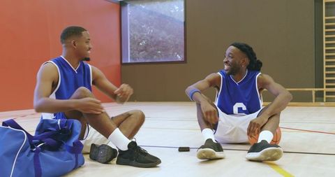 African american basketball players resting and laughing on indoor court after practice