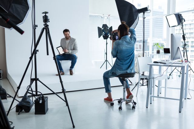 Male model posing for a professional photographer in a modern studio with lighting equipment and camera setup. Ideal for use in articles or advertisements related to fashion, professional photography, creative workspaces, or technology in photography.
