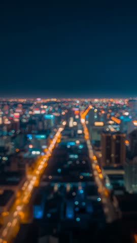 Drone recording lit city grid at night with bokeh skyline, vertical aerial nightscape