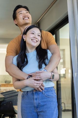Young diverse couple hugging and smiling by sliding door in bright modern home interior