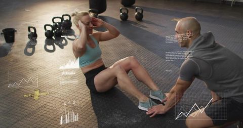 Female athlete performing crunches while trainer bracing feet with fitness metrics overlay