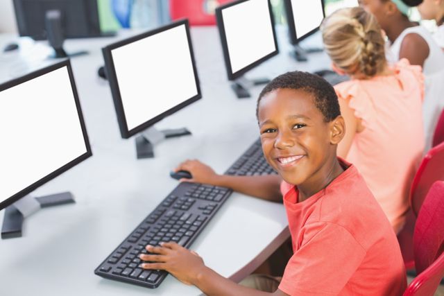 Young boy smiling while using computer in classroom, ideal for educational content, technology in education, school brochures, and digital learning resources.