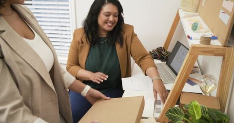 Female coworkers packing cardboard boxes and organizing online orders at small business desk consult