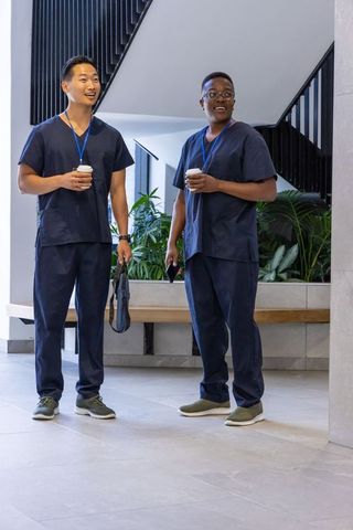 Two medical professionals chatting in modern lobby wearing navy scrubs and holding coffee