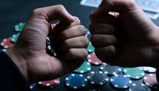 Clenched hands gripping black poker chip over felt table with scattered chips, tension
