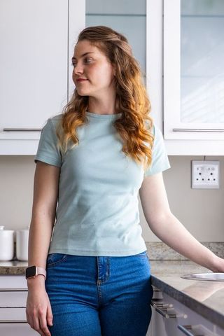 Young woman leaning on stone countertop wearing smartwatch and casual jeans in modern kitchen