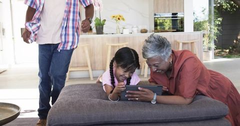Grandmother Sharing Tablet with Grandchild on Ottoman in Sunlit Modern Open-Plan Kitchen
