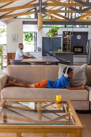 Father working remotely while son using tablet with headphones in open-plan living room