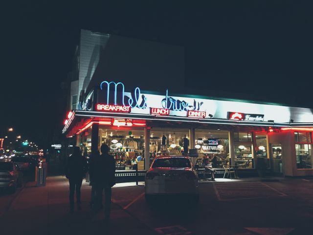 Retro diner glowing with neon lights at night, bringing nostalgic vibes of classic American eateries. Diners visible through windows, enjoying meals. Ideal for themes depicting vintage lifestyle, night scenes in urban environments, classic American food culture, or retro marketing promotions.