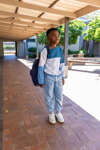 African american boy standing on sunlit school corridor with backpack and casual sneakers