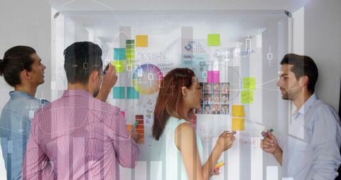 Creative team collaborating at glass board, brainstorming sticky notes for marketing design