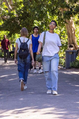 African american woman walking in sunlit park carrying green shoulder bag casual lifestyle