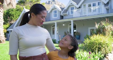 Mother and daughter smiling in front yard of suburban home with porch and balcony