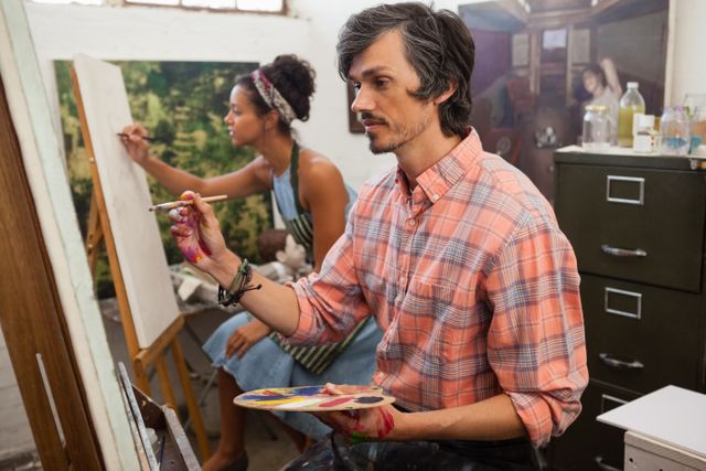 Man and woman painting on canvas in an art class. Both artists are focused on their work, using brushes and palettes. Ideal for illustrating creativity, teamwork, and artistic expression in educational or creative environments.