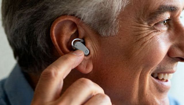 Senior man adjusting modern hearing aid while smiling, closeup of wearable tech