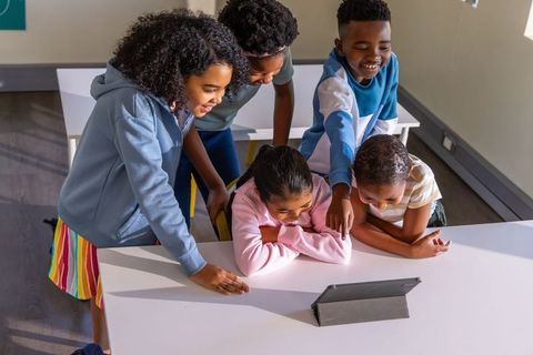 Children gathering around tablet watching educational video and collaborating in classroom