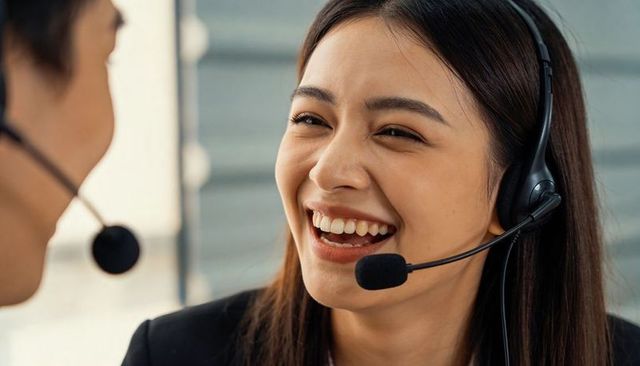 Smiling call center agent laughing during customer service call with headset and colleague