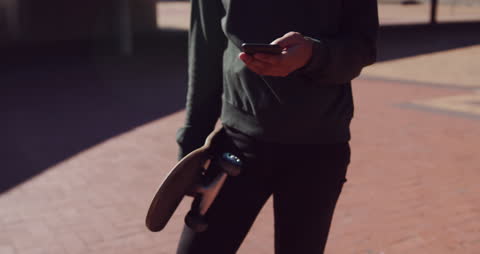 Trendy Individual Using Smartphone While Holding Skateboard