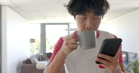 Young Male Student Multitasking with Coffee and Smartphone Indoors