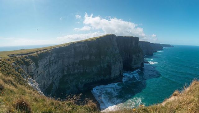 Windblown sea cliffs dropping into turquoise ocean with grassy plateau and coastal path