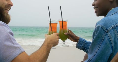 Smiling Couple Toasting Drinks at Oceanfront Beach