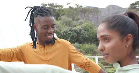 Smiling Black man and South Asian woman leaning on balcony railing enjoying mountain view
