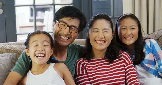 Smiling Asian family sitting together on couch at home. This image can be used for brochures, advertisements, websites, and articles focusing on family bonding, happy lifestyles, and home living.