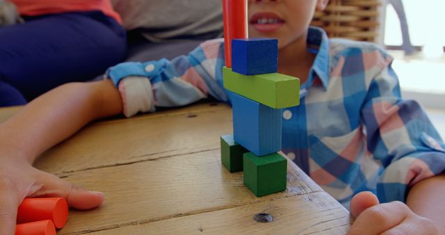 Biracial boy playing with colorful blocks, wearing plaid shirt. His hands show, focusing on assembling pieces on a wooden table