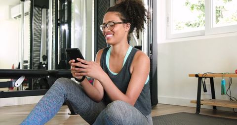 African American woman checking smartphone while resting after workout in home gym