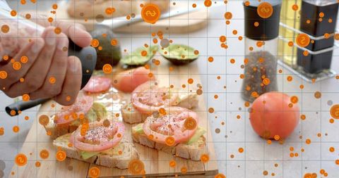 Hand sprinkling pepper over avocado tomato toasts on wooden cutting board for brunch