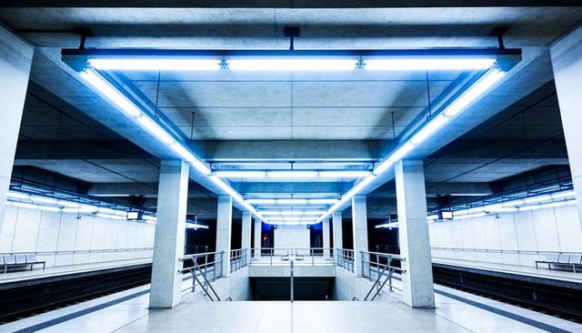 Futuristic symmetrical blue-lit underground metro platform with concrete columns and stairs
