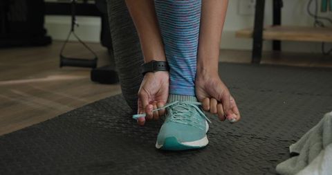 Woman tying teal running shoe laces on mat preparing for home workout