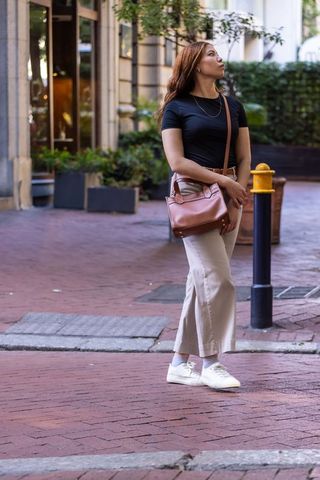 African american woman standing on brick street with brown crossbody bag looking up