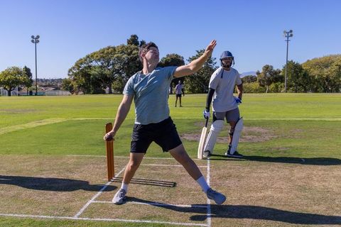 Club cricketer bowling delivery while batsman preparing at crease on sunny cricket field