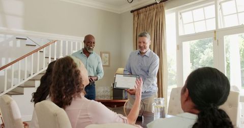Senior Man Holding Award While Diverse Friends Applaud at Home Gathering